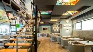A modern interior with a wooden herringbone floor, a staircase with metal railings, and a seating area with tables and chairs. - Mava Apartamente (Constanta)