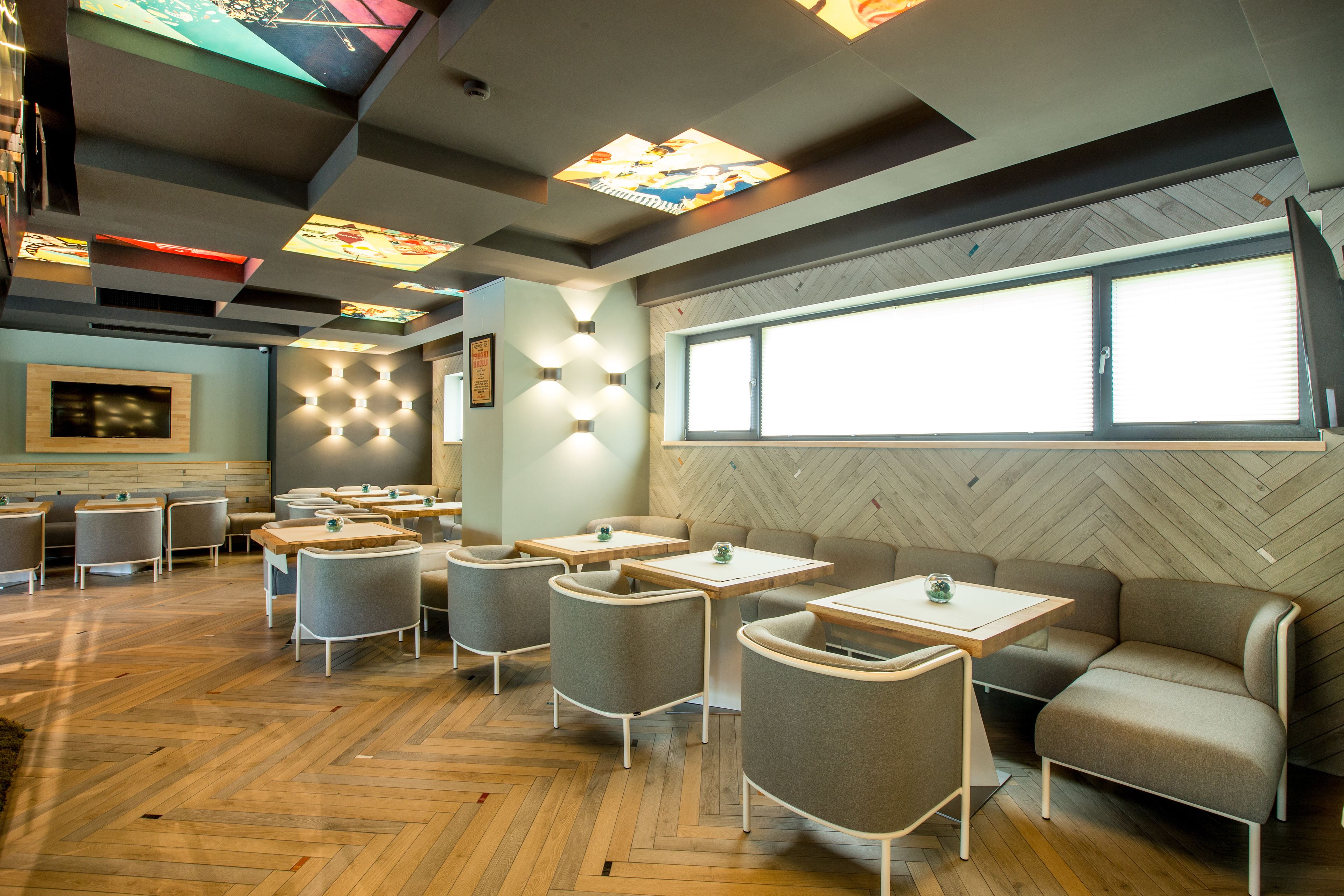 Ein modernes Restaurant mit Holzboden, grau gepolsterten Sitzmöglichkeiten und einer Wand mit Zickzackmuster.