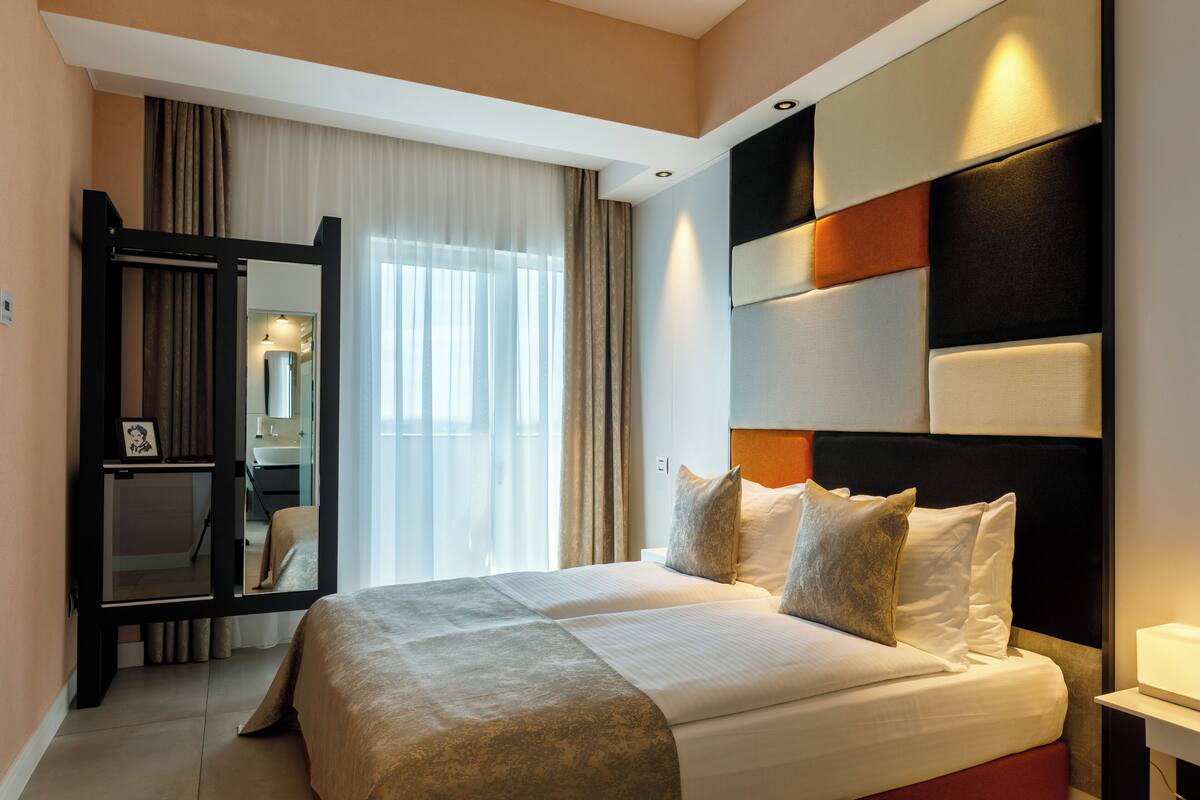 A hotel room with a large bed, a mirror, a bedside table, and a view of a bathroom.