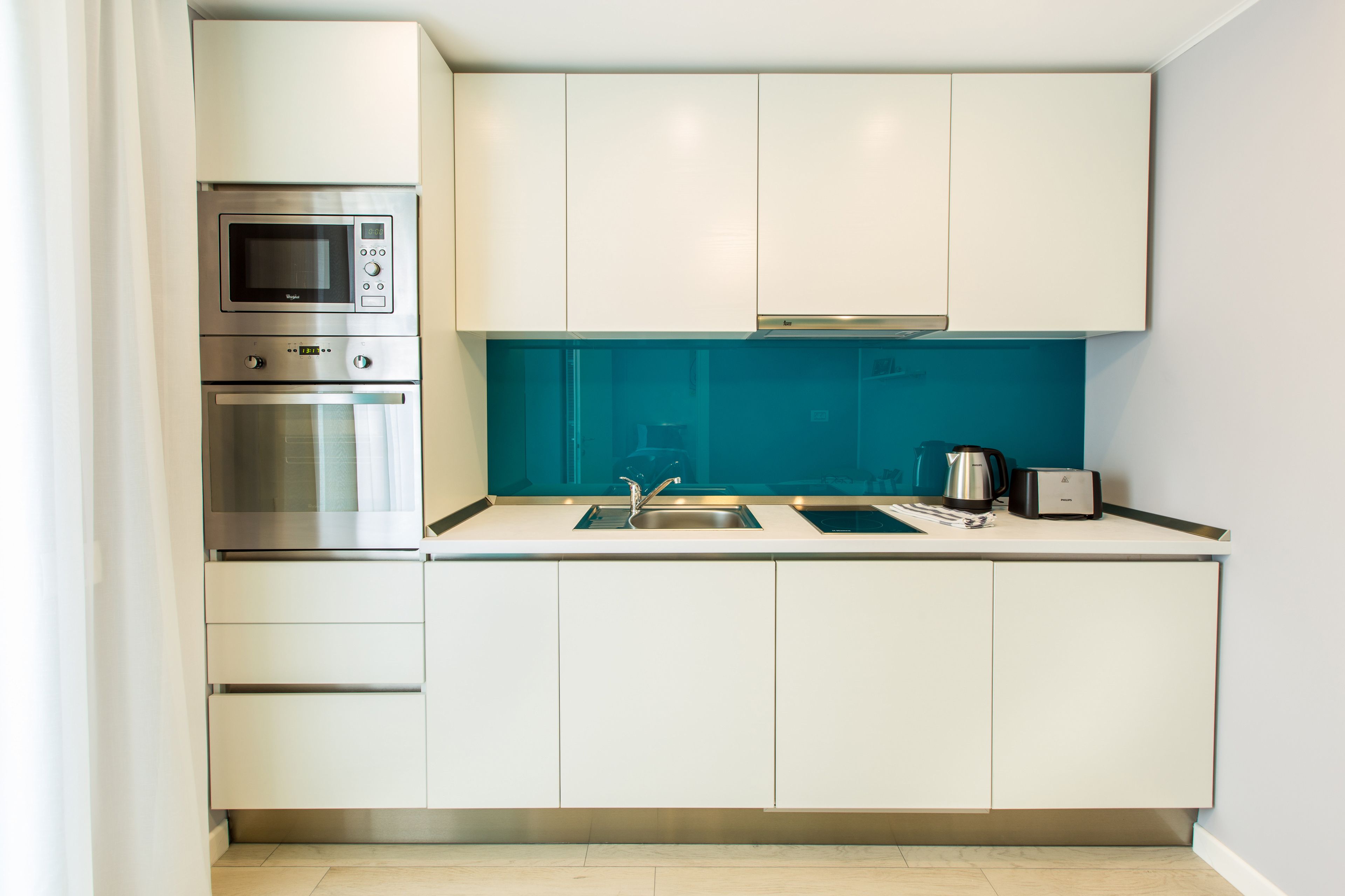 Una cocina moderna con armarios blancos, microondas integrado, horno y salpicadero azul.