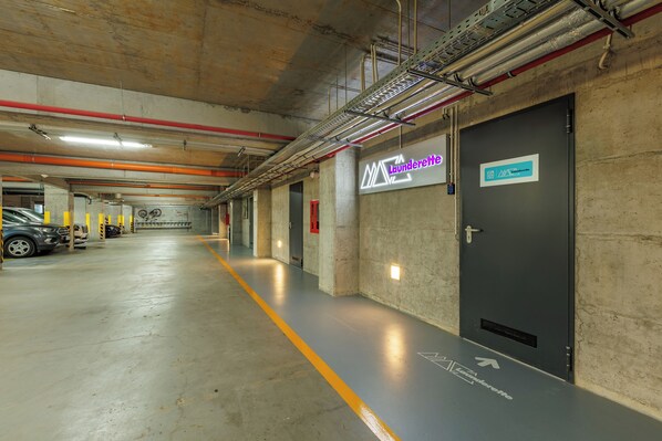 Un parking avec des murs en béton, une ligne jaune indiquant la sortie et un panneau indiquant « Laverie ».