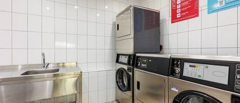 A modern laundry facility with stainless steel appliances, a sink, and informational posters on the wall.