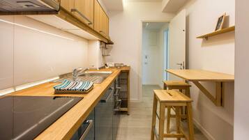 Una cocina moderna con armarios de madera, un lavamanos de acero inoxidable y un horno empotrado. Hay taburetes de madera y una pequeña mesa.