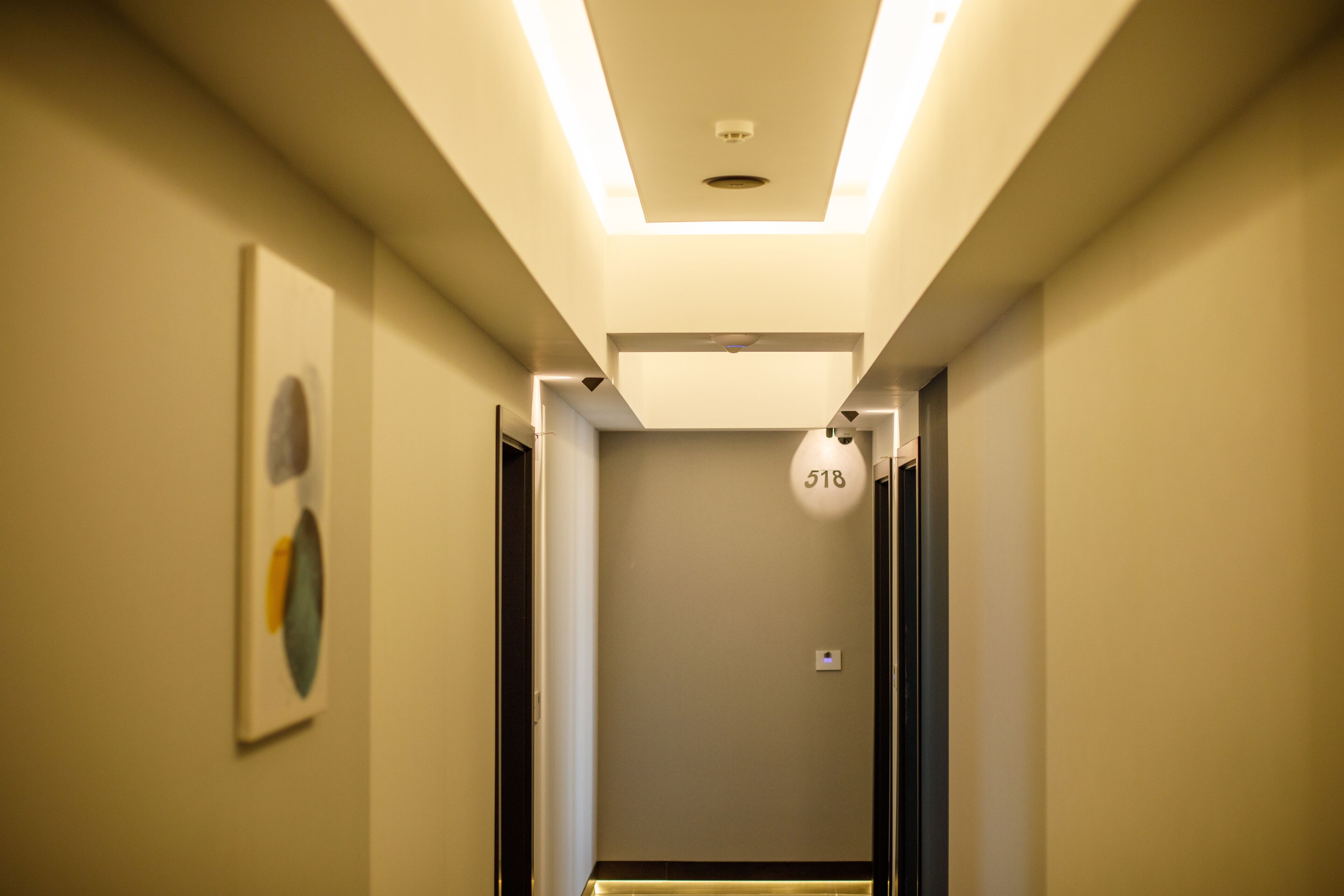 A modern hallway with a ceiling light, a number sign, and a framed artwork on the wall.
