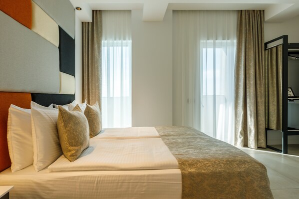 A hotel room with a large bed, two windows with sheer curtains, and a wardrobe.