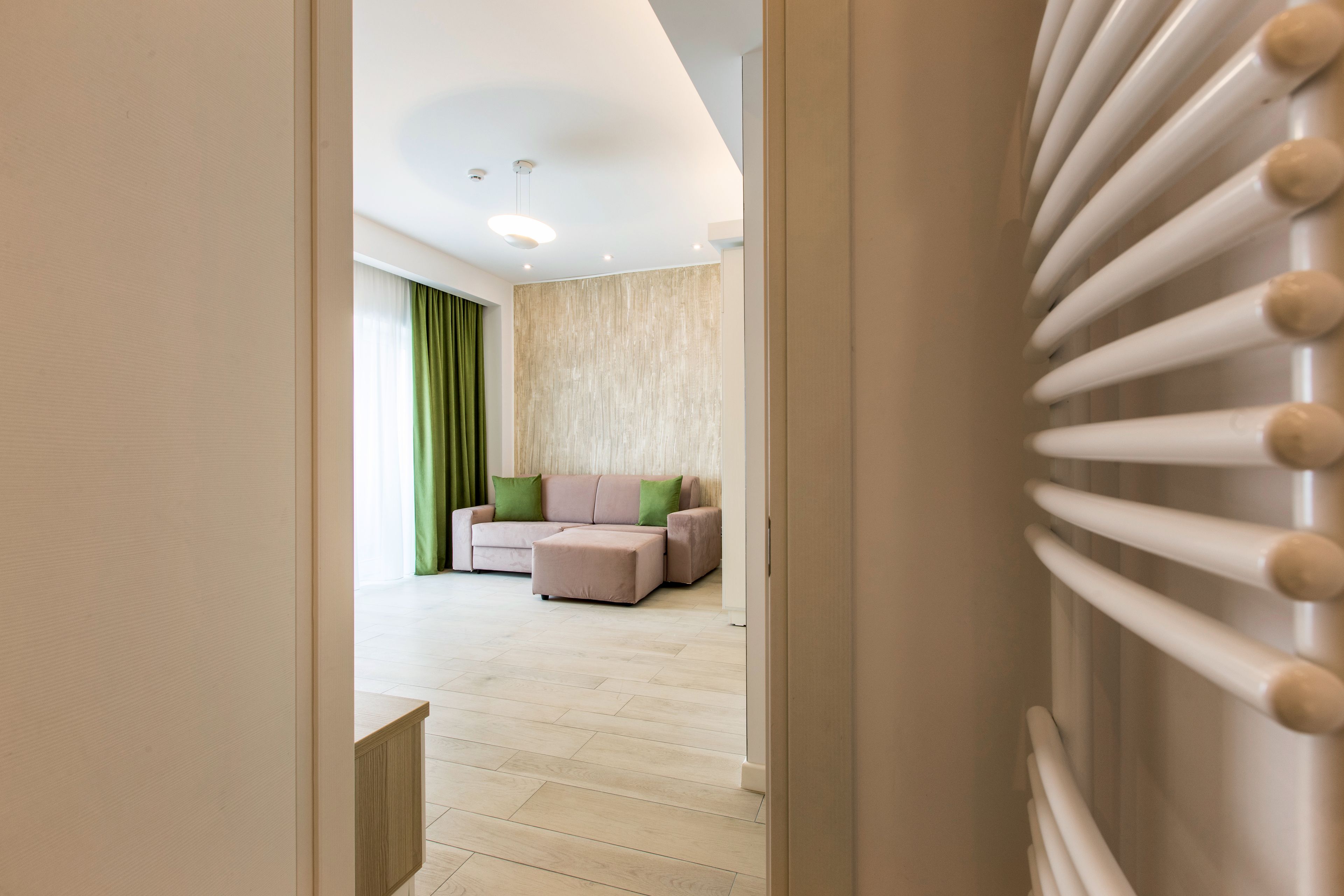 Una sala de estar moderna con un sofá y un reposapiés, suelo de madera y una cortina verde.