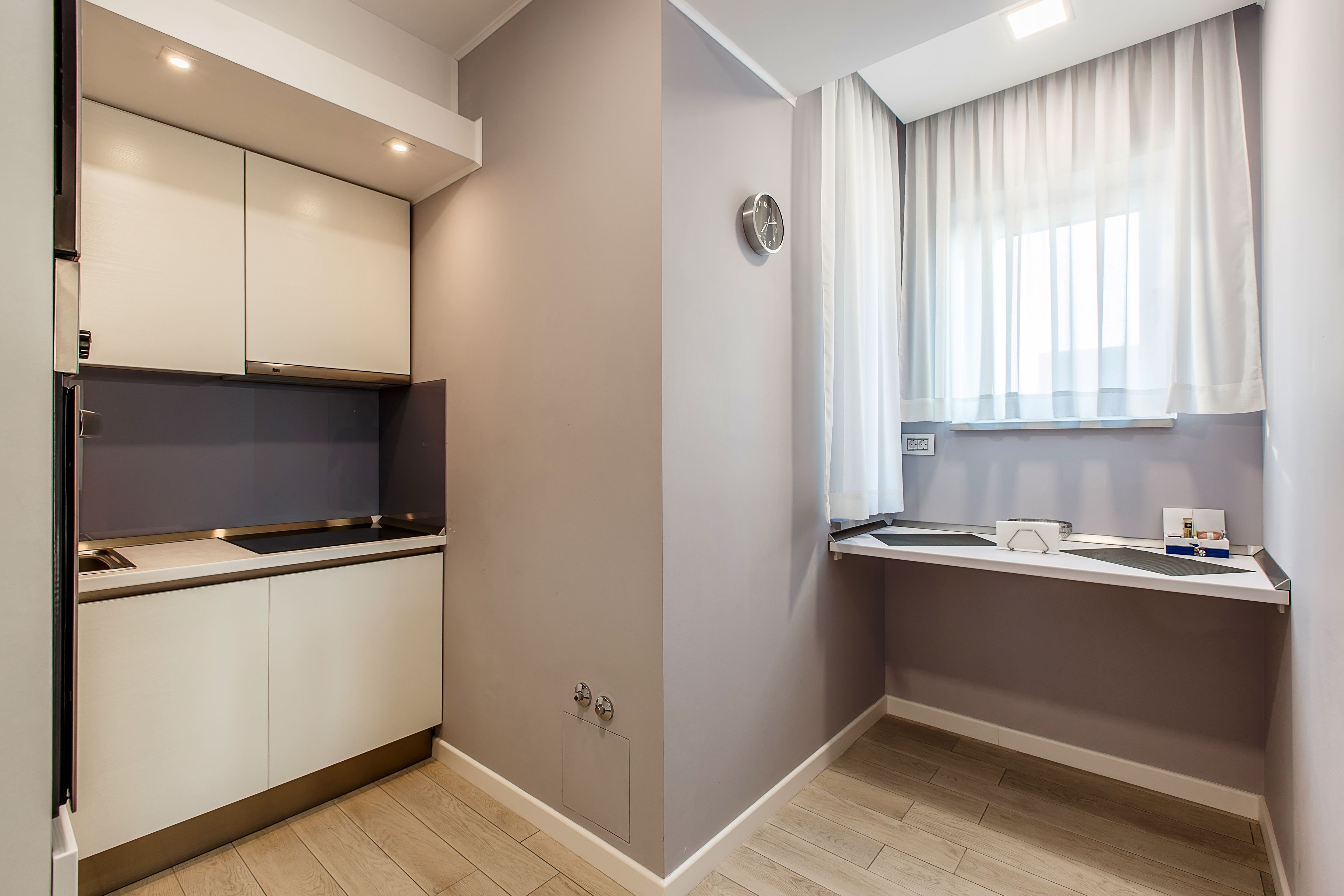 A modern kitchen with white cabinets, a built-in oven, and a window with sheer curtains.