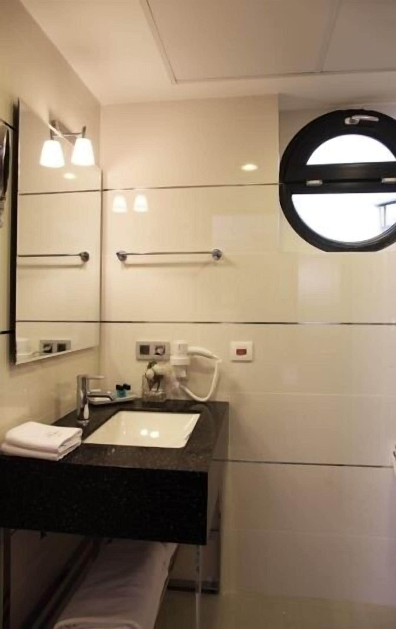 A modern bathroom with a large mirror, a round window, and a black countertop.