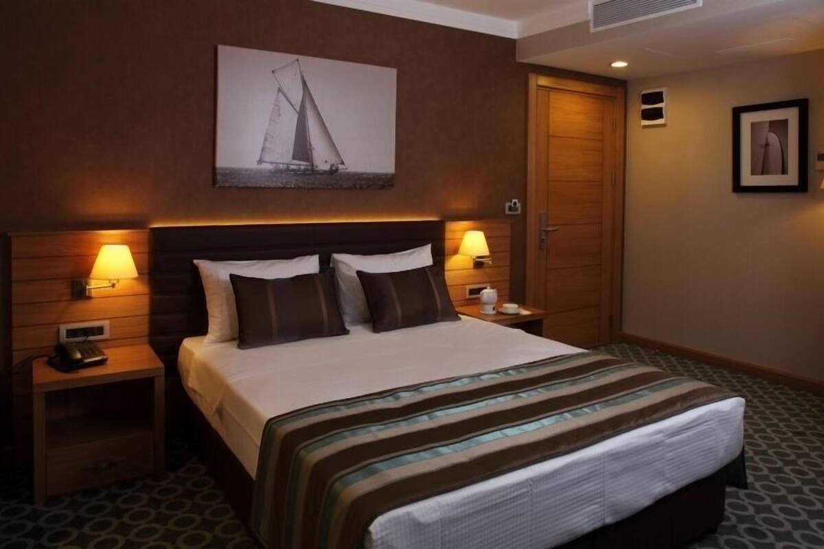 A hotel room with a bed, two bedside tables with lamps, a framed picture on the wall, and a door.