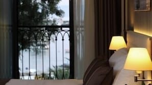 A hotel room with a bed, two bedside lamps, a vase with flowers, and a view of the outdoors through a window with a metal railing. - Tuzla Town Hotel (Tuzla)
