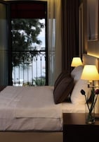 Habitación de hotel con una cama, dos lámparas de noche, un jarrón con flores y vistas al exterior a través de una ventana con barandilla de metal.