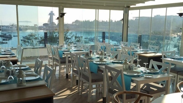 A restaurant with tables set for dining, large windows offering a view of the sea and boats. - Tuzla Town Hotel (Tuzla)
