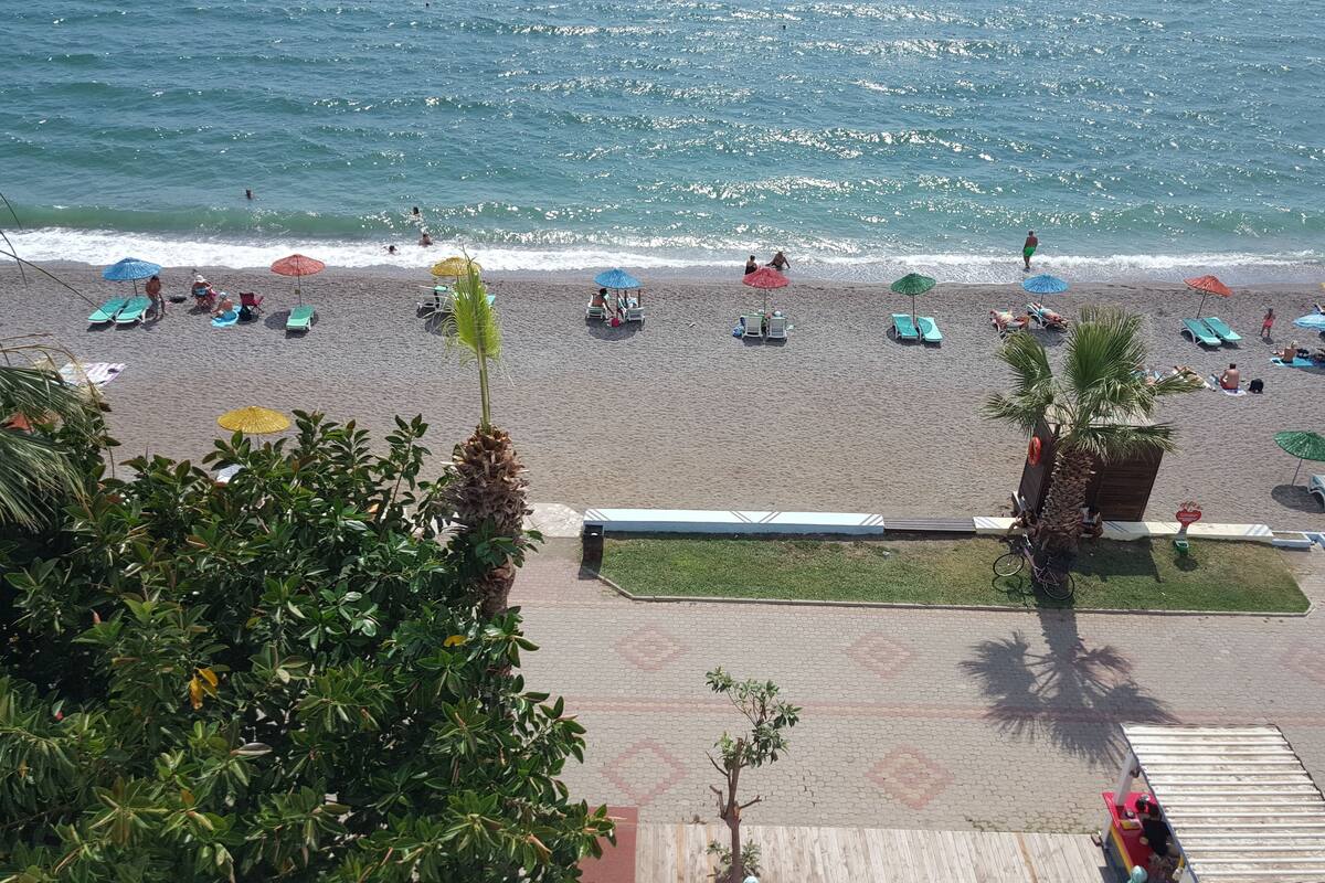 A beach with sun loungers and umbrellas, a wooden deck, and a view of the ocean.