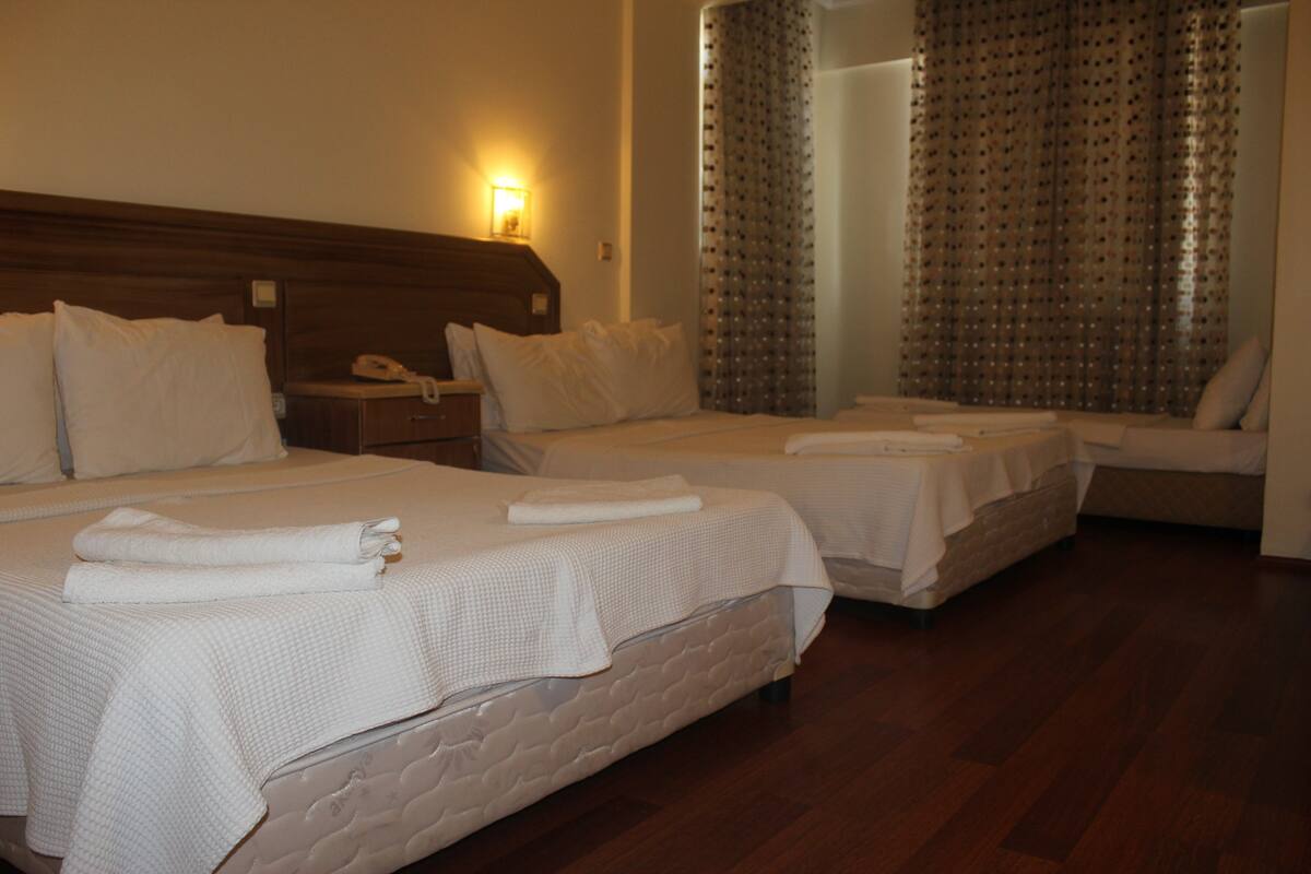 A hotel room with two beds, a wooden headboard, a bedside table with a lamp, and a mirror.