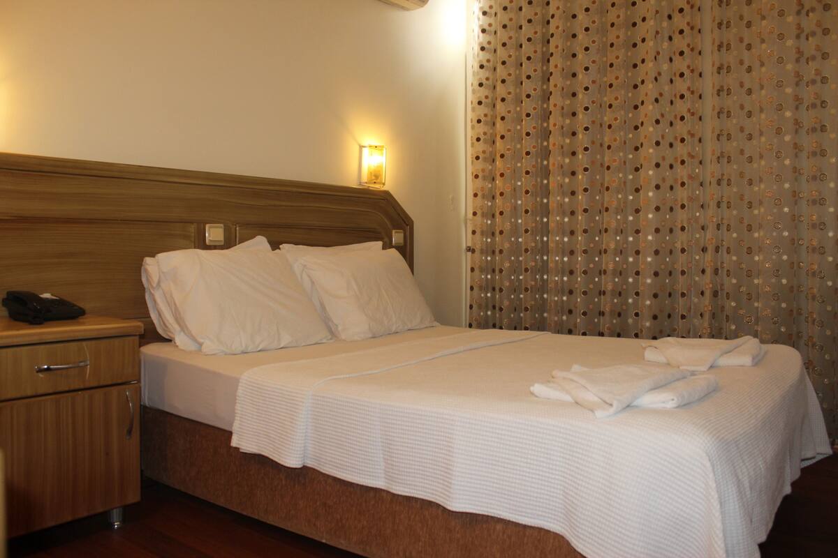 A hotel room with a wooden headboard, a single bed with white linens, a bedside table with a phone, and a curtain with a polka dot pattern.