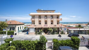 A multi-story hotel with a central atrium, outdoor seating, and a view of the sea. - Hotel Eden (Rimini)