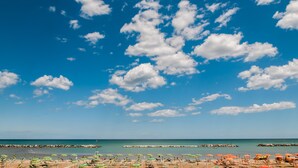 A beach with umbrellas and beach chairs, a clear sky, and calm water. - Hotel Eden (Rimini)