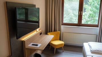 Habitación de hotel con cama, escritorio con silla, televisor montado en la pared y ventana con cortinas.