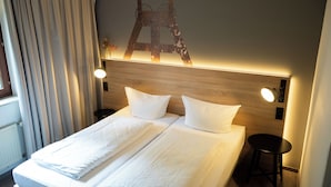 Ein Doppelbett mit weißer Bettwäsche, einem hölzernen Kopfteil, Nachttischlampen und einem kleinen Tisch.