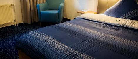 A hotel room with a bed, a chair, a nightstand, and a lamp.