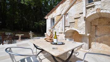 Eine Außenpatio mit einem Steintisch und Metallstühlen, einer Weinflasche und einem rustikalen Steinhaus im Hintergrund.