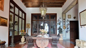 A traditional interior with a wooden ceiling, a chandelier, a dining table with chairs, and a large window with glass panes.