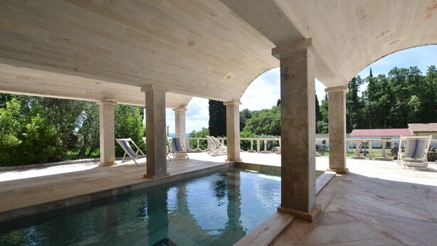 An indoor swimming pool with a covered area, columns, and lounge chairs.