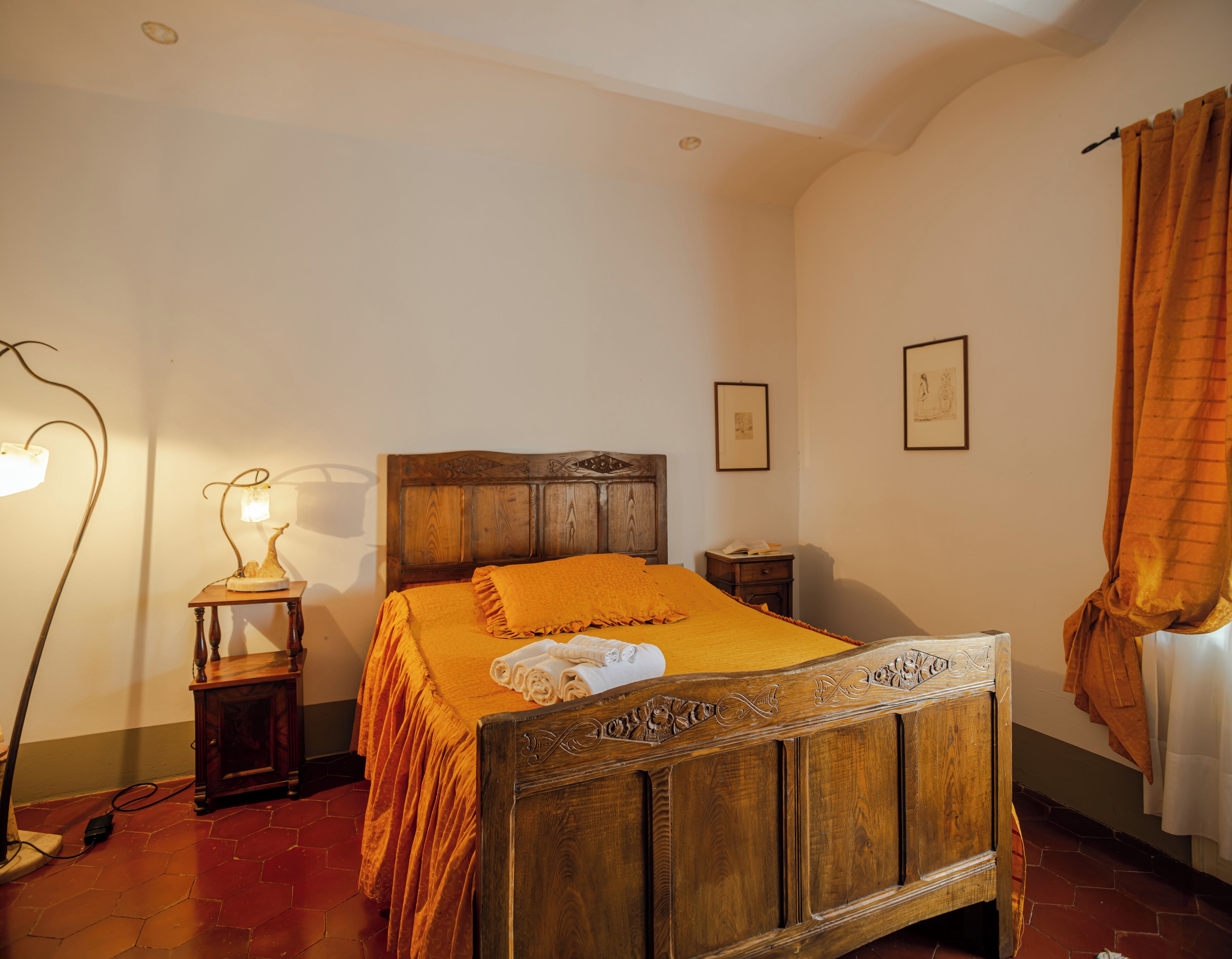 A bedroom with a wooden bed, a nightstand, a floor lamp, and a window with curtains.