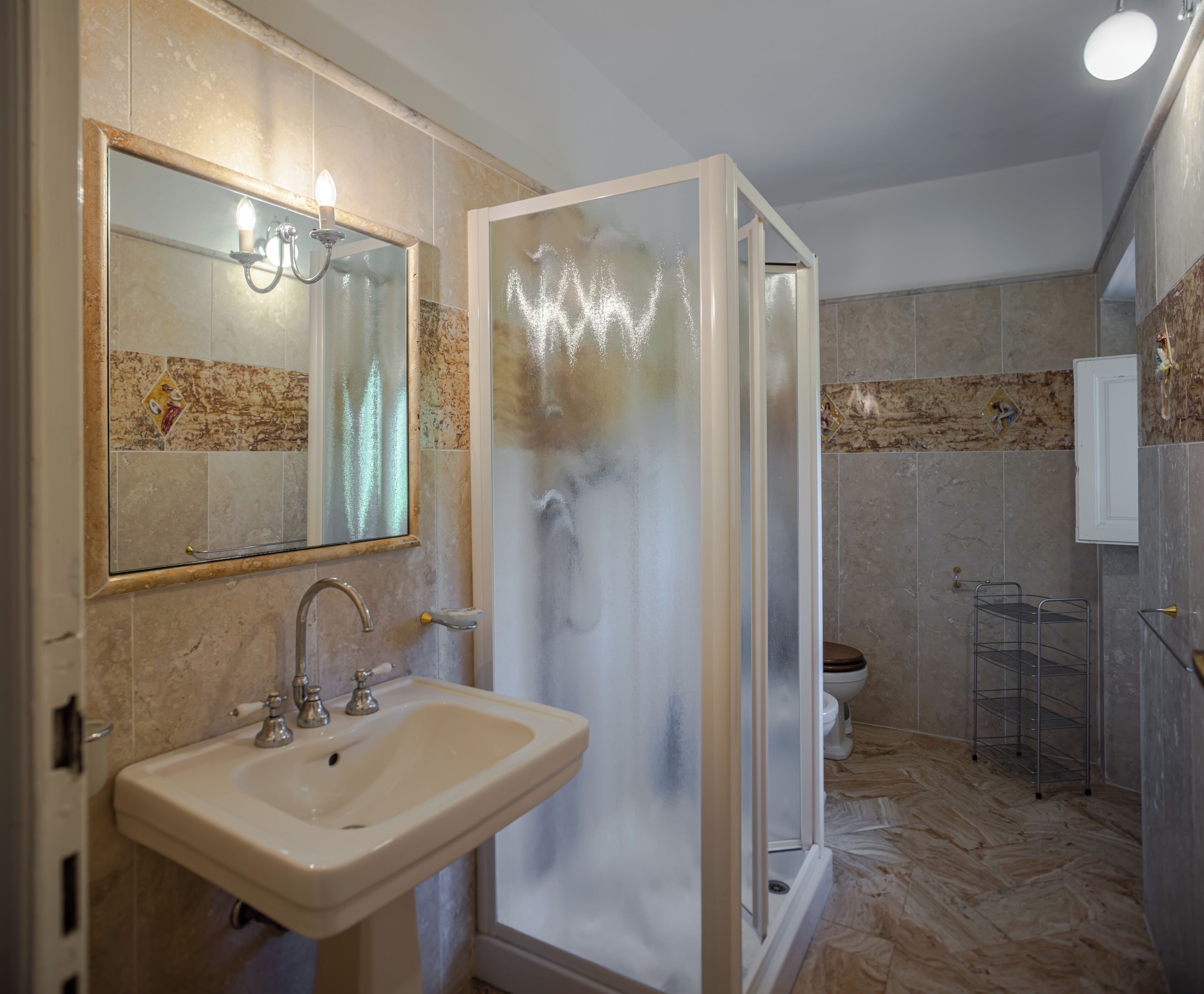 A bathroom with a sink, mirror, shower enclosure, and tiled walls.