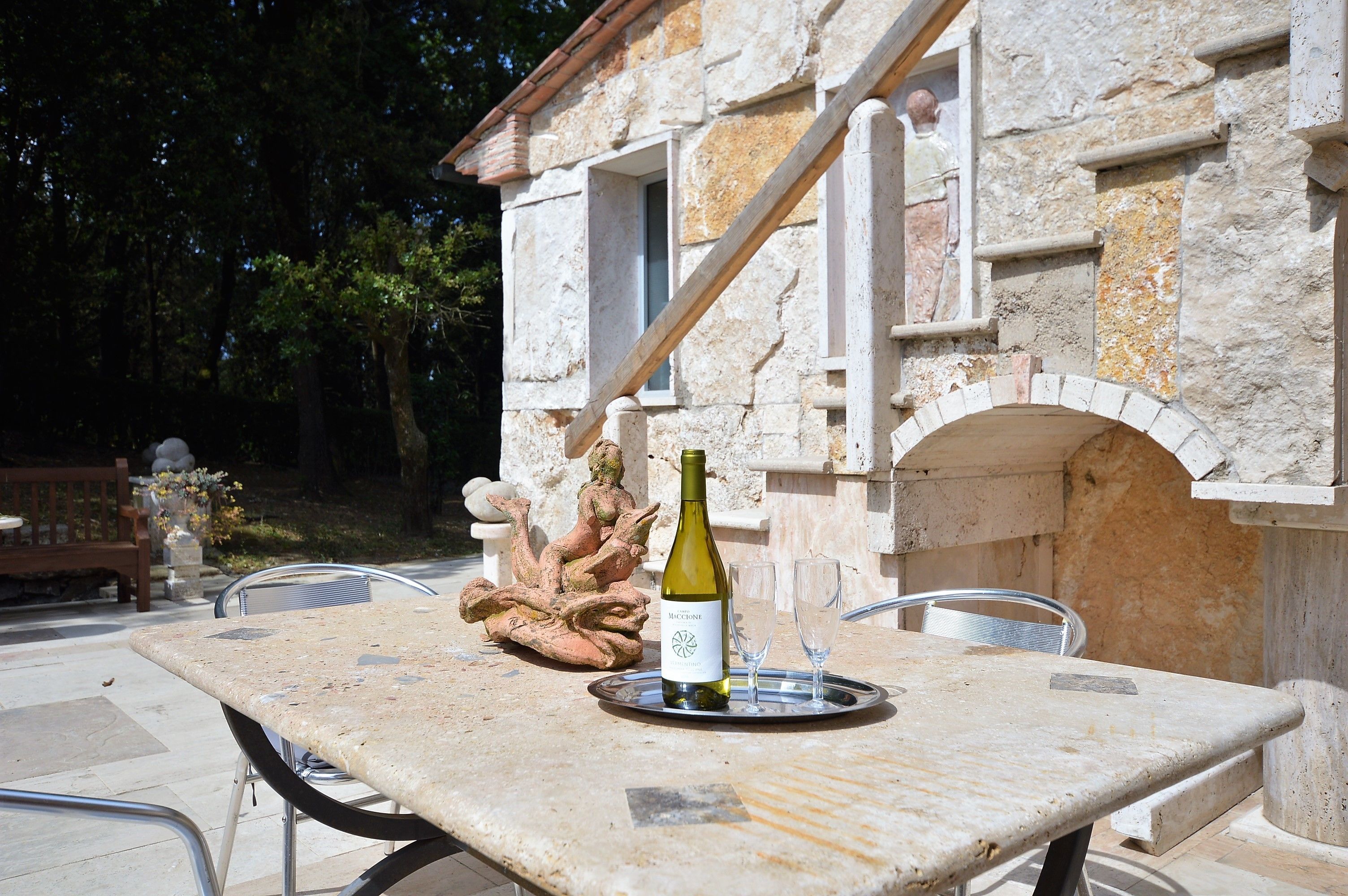 An outdoor stone building with a table and chairs, a bottle of wine, and a decorative sculpture.