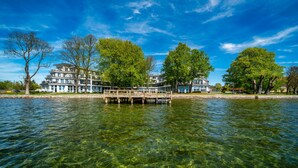 Un hôtel situé au bord de l’eau, doté d’un quai s’avançant dans l’eau, et entouré d’une végétation luxuriante sous un ciel bleu azur.