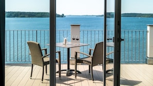 Un balcon avec des fauteuils en osier et une table, donnant sur une étendue d’eau calme, avec une côte lointaine à l’horizon.
