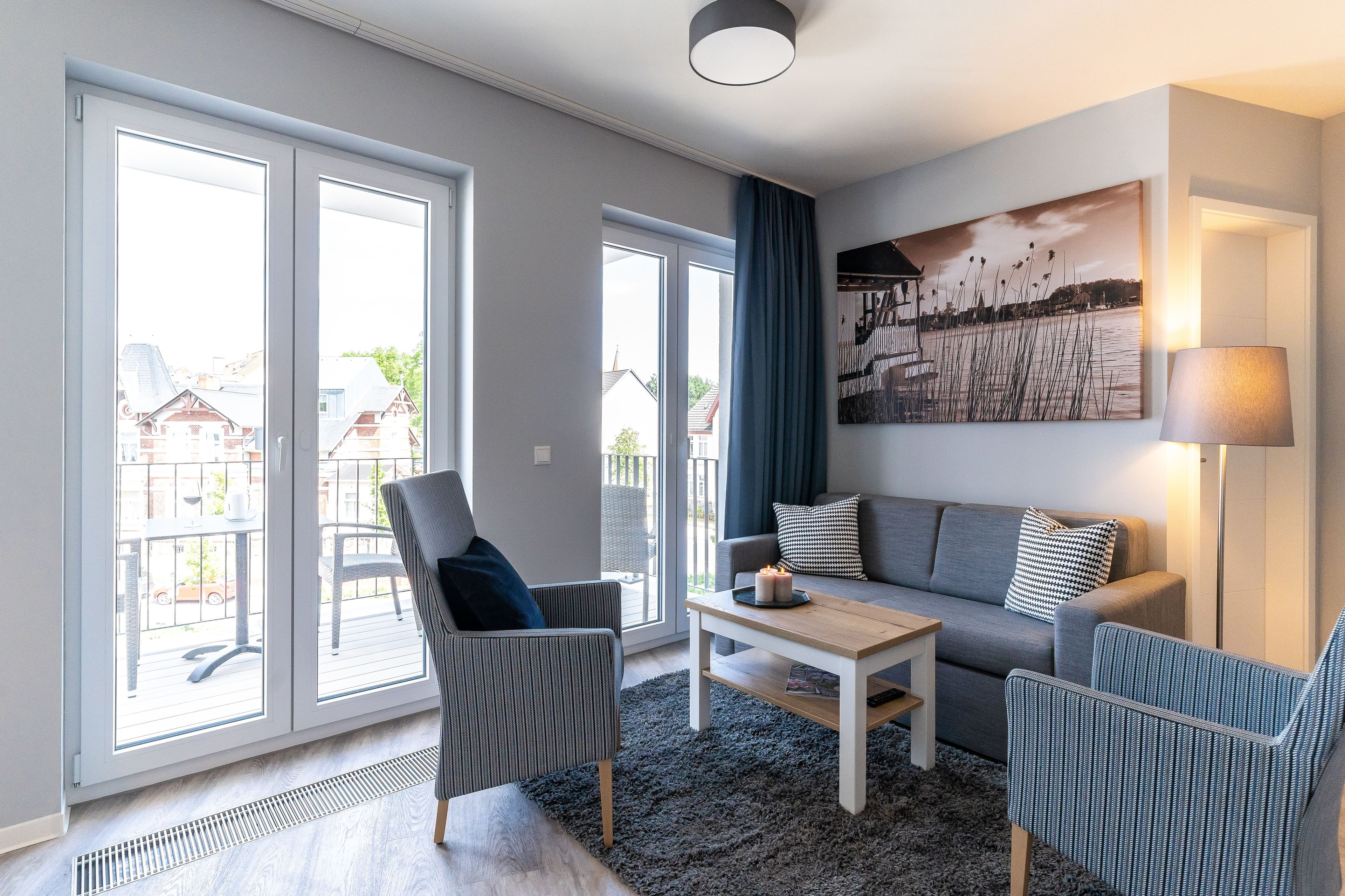A modern living room with a grey sofa, two armchairs, a coffee table, and a large window with a view of houses.