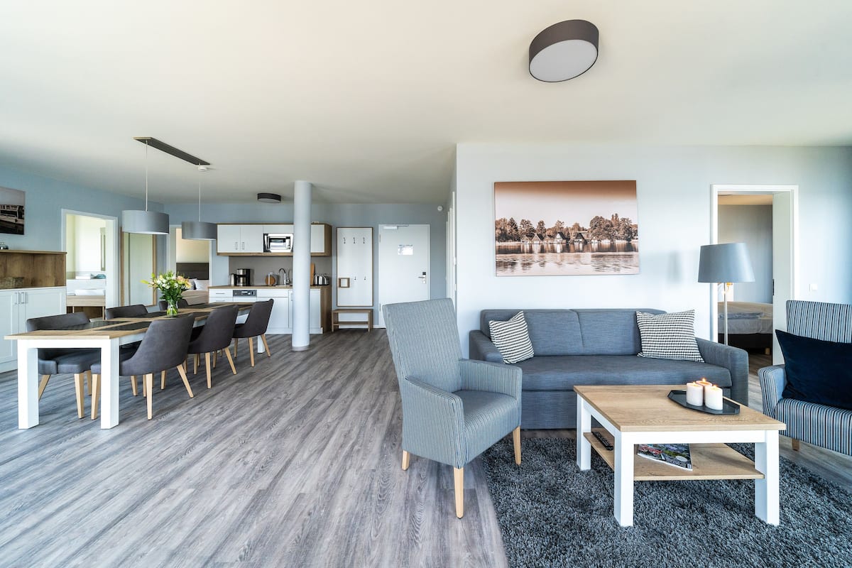 Uma sala de estar moderna com um sofá cinzento, uma mesa de centro e um espaço de jantar com uma mesa e cadeiras de madeira.