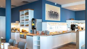 A modern cafe with a blue and white color scheme, featuring a counter with food and drinks, a coffee machine, and a cityscape artwork on the wall.