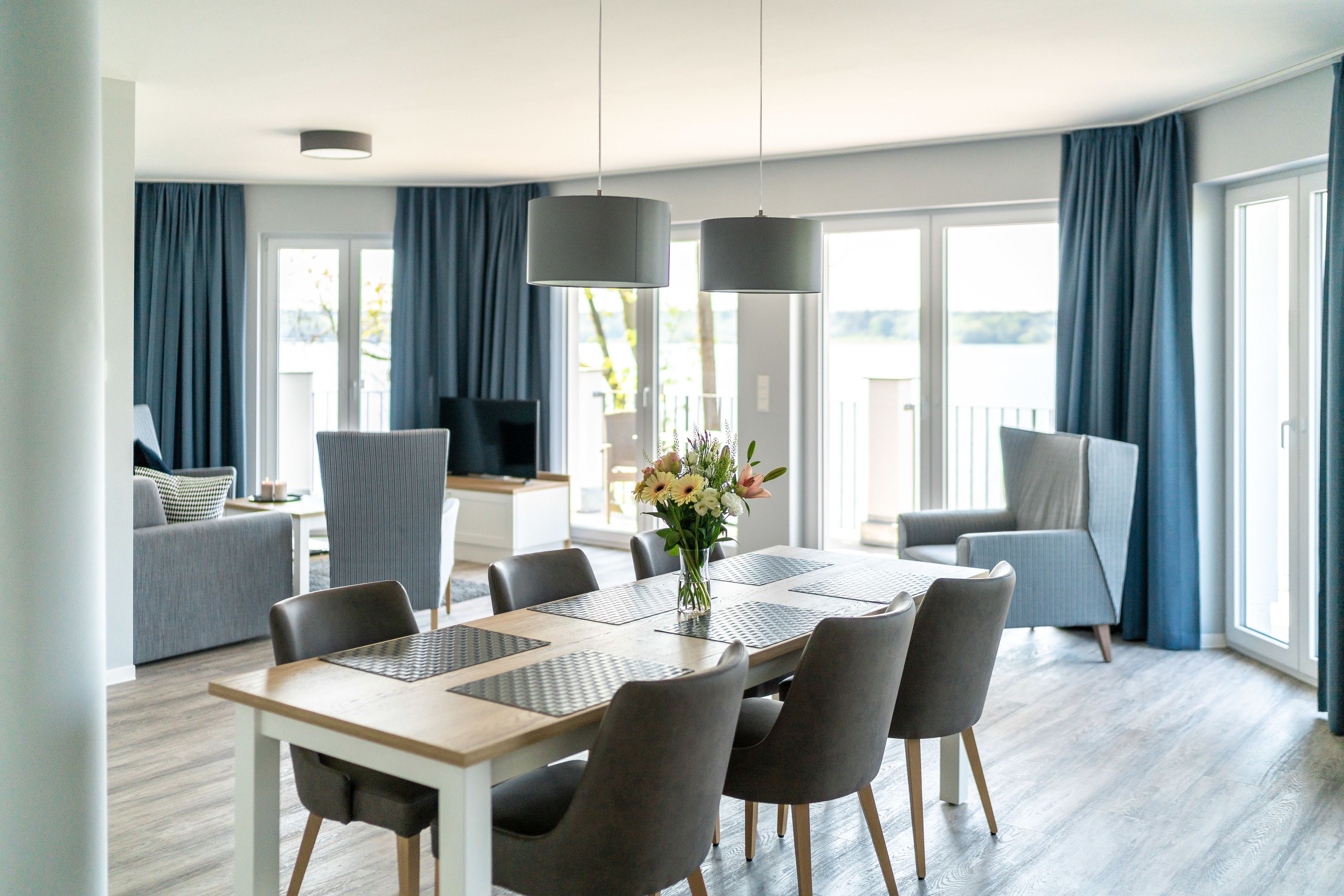 A modern dining area with a wooden table, grey chairs, and a vase of flowers.