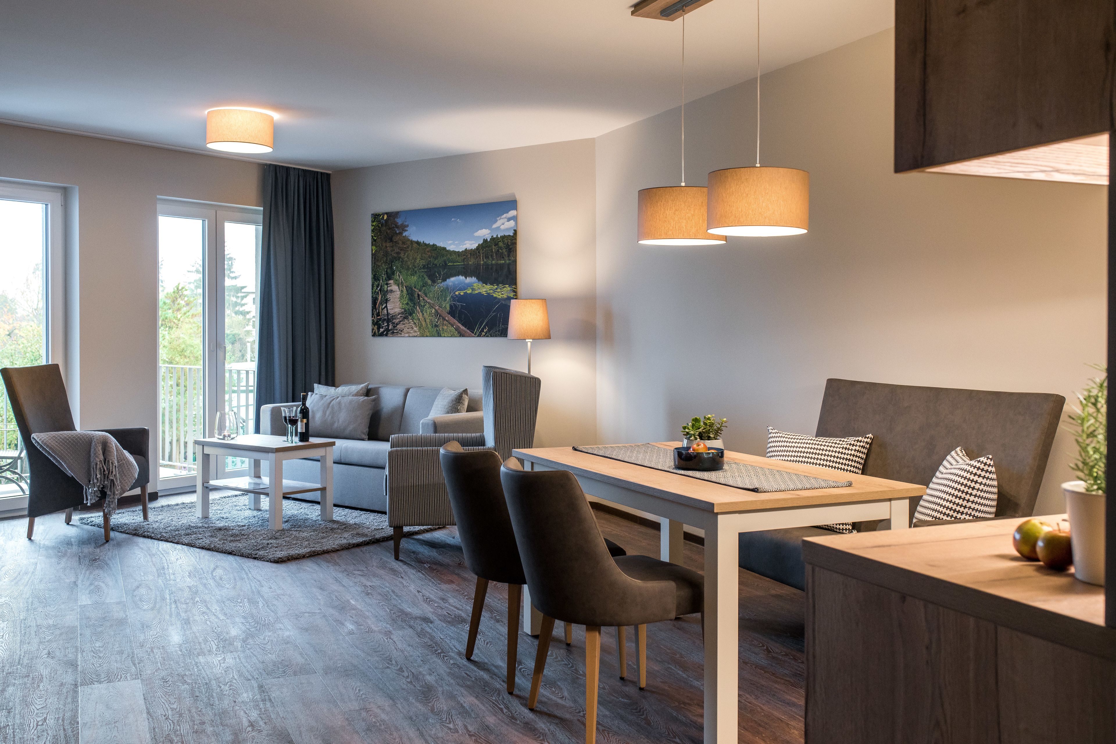 Un salon moderne comprenant un canapé, des fauteuils, une table à manger et une grande fenêtre donnant sur un lac.