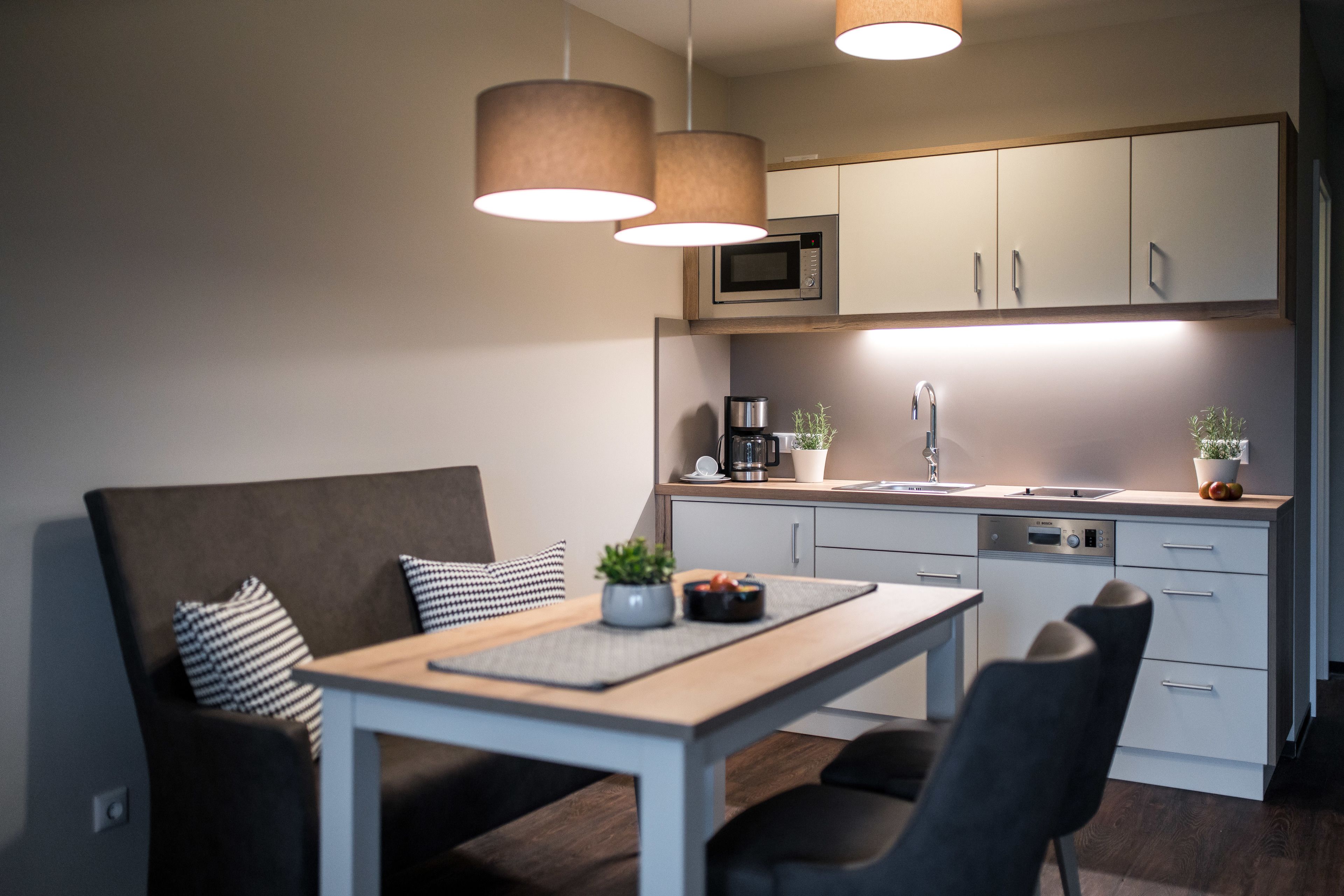 A modern kitchen with a dining area, featuring a microwave, coffee maker, sink, and cabinets.