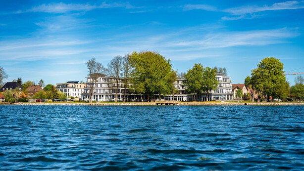 Un hôtel situé au bord de l’eau, composé de plusieurs bâtiments, doté d’un quai et bordé d’arbres.