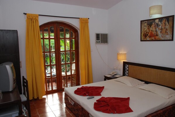 A hotel room with a bed, a desk with a telephone, a painting on the wall, and a window with curtains. - Sea Breeze Beach Resort Candolim (Candolim)