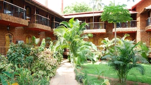 A courtyard with a pathway surrounded by lush greenery and a brick building with multiple balconies.