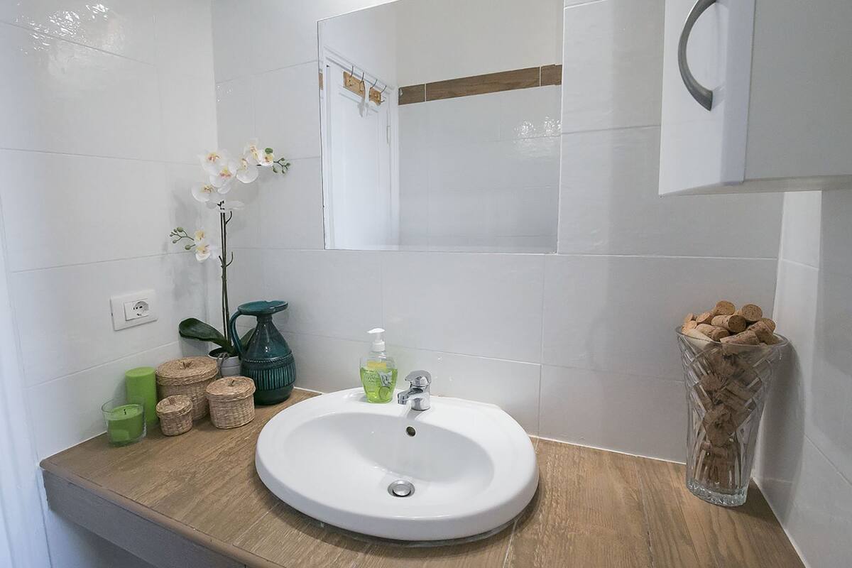 Un bagno con un lavandino bianco, un dispenser di sapone verde e un vaso con dei tappi di sughero.