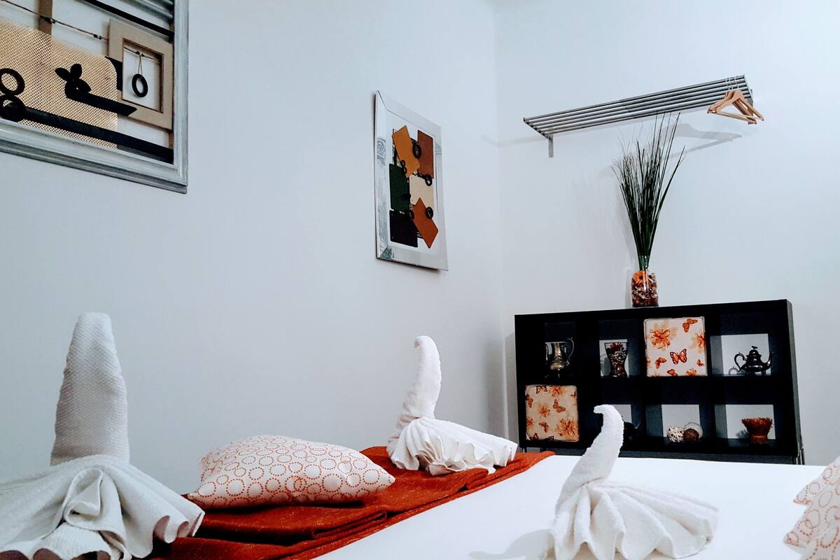 Una camera d'albergo con un letto rifatto, una mensola nera con soprammobili e un condizionatore d'aria a parete.