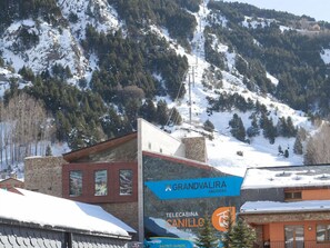 A hotel sign with 'GRANDVALIRA' and 'CANILLO' branding, surrounded by snow-covered mountains and trees.