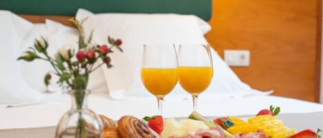 A breakfast setup with croissants, strawberries, cheese, and a fruit plate on a wooden table. Two glasses of orange juice are also visible.