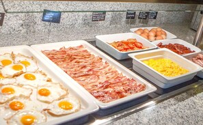 A buffet with various food items including bacon, eggs, and sausages.