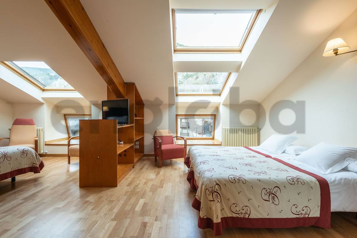 A bedroom with a loft bed, a TV on a wooden shelf, and skylights.