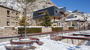 Un patio cubierto de nieve con un banco de madera, un muro de piedra y un edificio con balcones.
