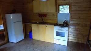Pieni, käytännöllinen keittiö, jonka seinät ovat puuta, ja jossa on valkoinen jääkaappi, liesi ja pesuallas.