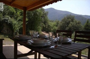 A wooden table set outdoors with plates, glasses, and cutlery, overlooking a mountainous landscape. - Camping Manso Coguleras (Santa Pau)
